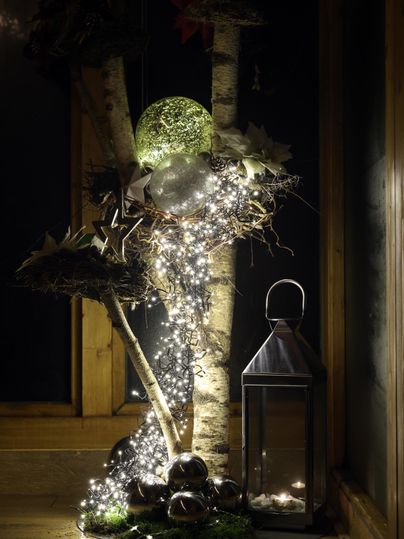 A festive decoration with a tree adorned with lights and ornaments. Next to the tree stands a lantern that creates a cozy atmosphere.