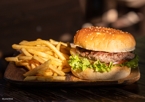 Een sappige burger met sesambroodje, sla en tomaat ligt op een houten plank. Naast hem liggen knapperige frietjes.