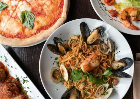 Ein Tisch mit verschiedenen italienischen Gerichten: Pizza Margherita, Spaghetti mit Meeresfrüchten und Fleischbällchen in Tomatensauce.