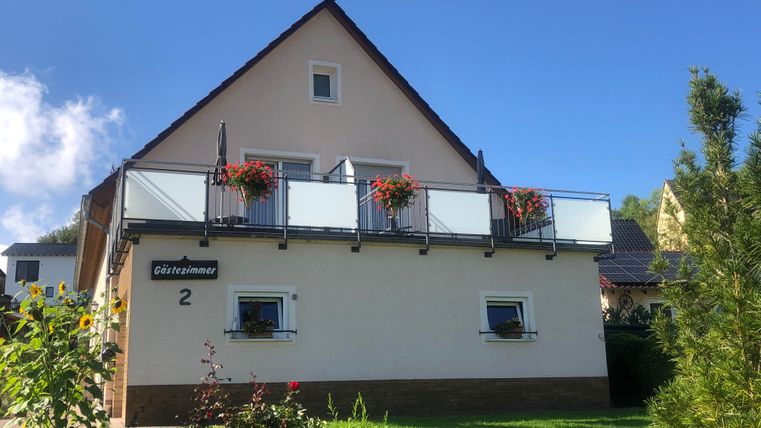 Ein schönes Haus mit einem Balkon und Blumenkästen. Der Garten ist grün und gepflegt, und der Himmel ist klar und blau.