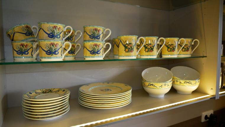A shelf with colorful dishes. On the top are cups with floral patterns, and on the bottom are plates and bowls.
