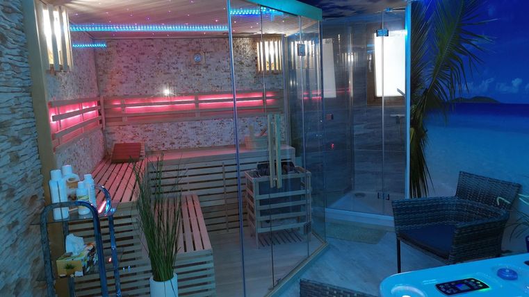 Ein moderner Wellnessbereich mit einer Sauna und farbigen Lichtern. Entspannungsecken mit bequemen Stühlen runden die Atmosphäre ab.