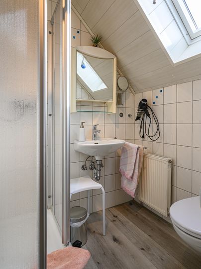 Ein kleines Badezimmer mit Dusche, Waschbecken und Toilette. Es hat helle Fliesen und ein Fenster, das natürliches Licht hereinlässt.