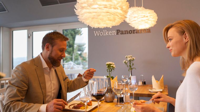 Een elegant restaurant met een stel dat samen van het eten geniet. De sfeer is warm en uitnodigend, met moderne lampen en uitzicht naar buiten.