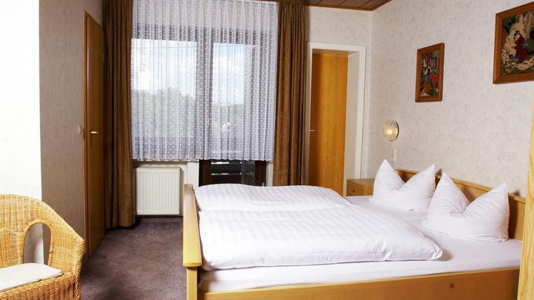 A simple bedroom with a double bed and two pillows. A cozy armchair and large windows provide plenty of light.