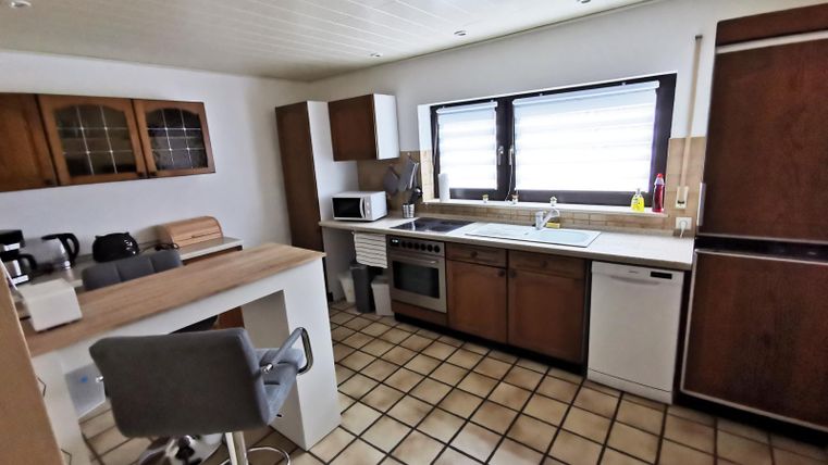 A modern kitchen with wooden cabinets and bright tiles. The room design is open and inviting, ideal for preparing meals.