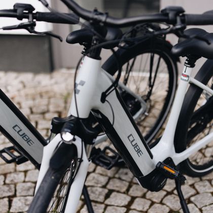 Zwei moderne Fahrräder der Marke Cube stehen nebeneinander auf einem gepflasterten Boden. Sie haben ein elegantes Design in Weiß und Schwarz.