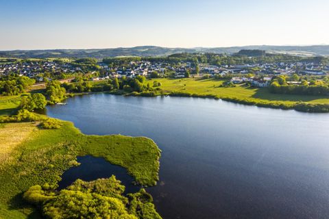A picturesque landscape with a calm lake and green meadows. In the background, small houses and hills can be seen.