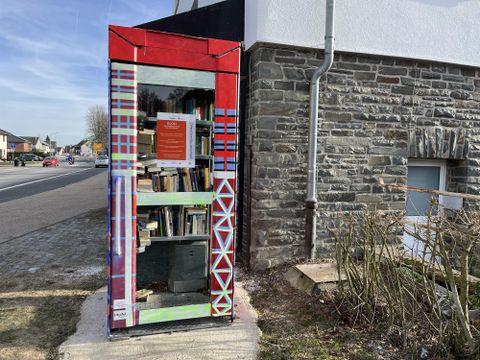 Een kleurrijke boekenbox staat op de straathoek naast een gebouw. Ze is gevuld met verschillende boeken en biedt leesmogelijkheden voor voorbijgangers.