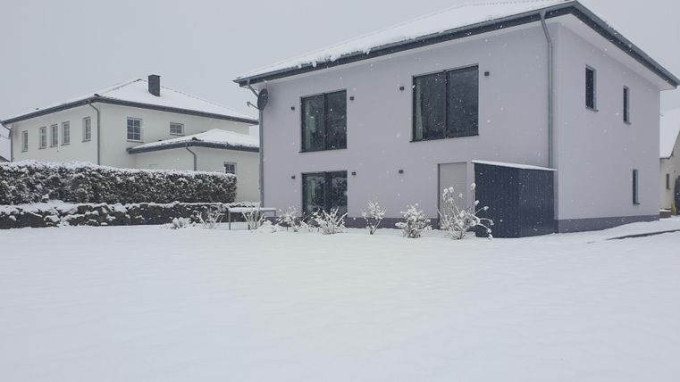 Ein modernes Haus inmitten einer verschneiten Landschaft. Der Garten und die Umgebung sind völlig mit Schnee bedeckt.