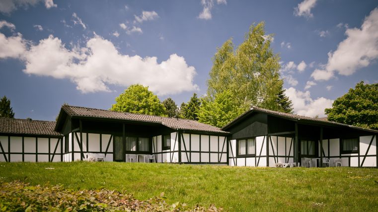 Zwei gemütliche Ferienhäuser mit traditionellen Fachwerkwänden in einer grünen Umgebung. Der Himmel ist blau und mit wenigen Wolken geschmückt.