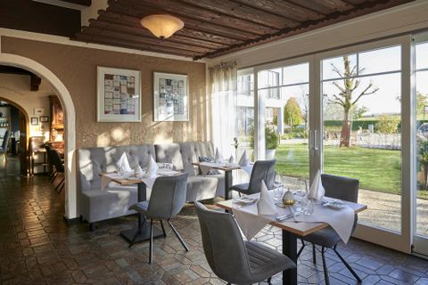 An inviting restaurant with elegant tables and chairs. Large windows offer a view of the outdoor area with green spaces.