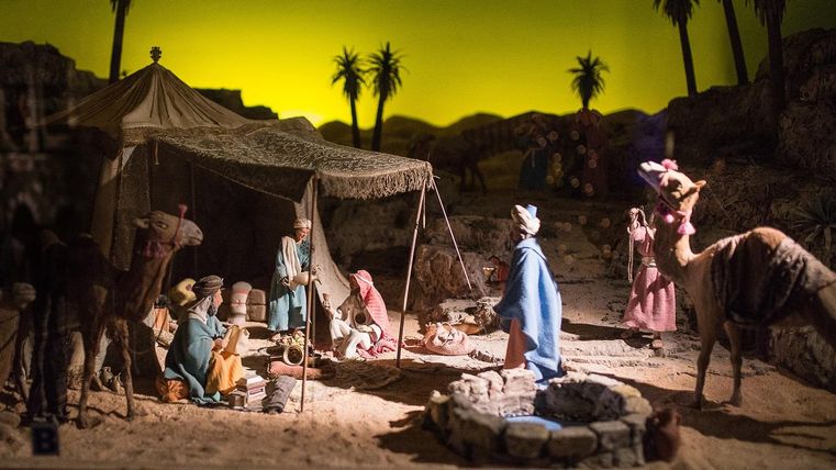 Eine Krippenszene mit Figuren in einer Wüstenlandschaft. Zelte, Kamele und Palmen sind im Hintergrund zu sehen.