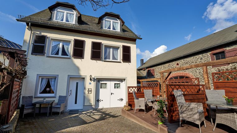 A modern house with a bright outdoor area and comfortable garden furniture. The sky is blue and sunny, creating an inviting atmosphere.