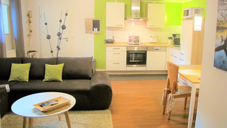 A modern apartment with a cozy living room and an open kitchen. The decor is bright and inviting, featuring a simple table and chairs.