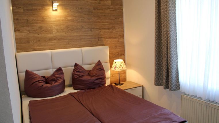 Ein gemütliches Schlafzimmer mit einem großen Bett und weichen Kissen. Die warmen Farbtöne und das sanfte Licht sorgen für eine entspannte Atmosphäre.