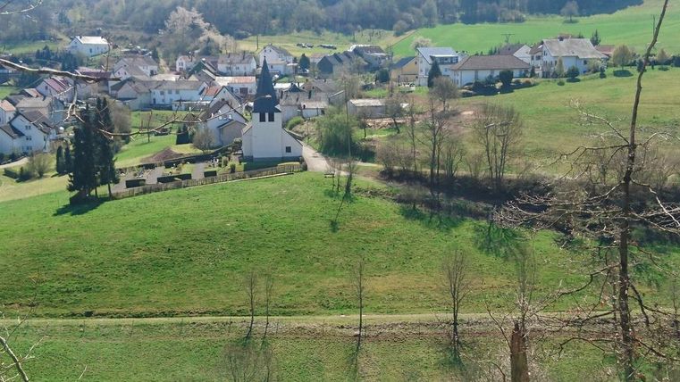 Een schilderachtig landschap met een klein dorp en een kerk. Omgeven door groene weilanden en zachte heuvels.
