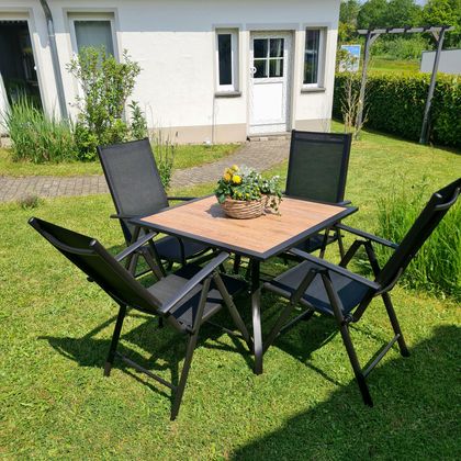 Ein gemütlicher Garten mit einem Tisch und Stühlen. Auf dem Tisch steht ein dekorierter Blumentopf.