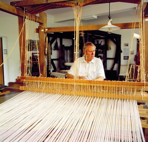 Een man werkt aan een weefgetouw in een werkplaats. De kleurrijke draden zijn klaar om te weven.