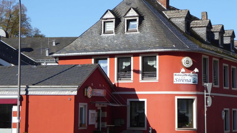 A red building with an interesting roof and windows. On the wall, there is a sign that reads "Sirena."
