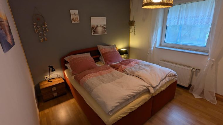 A cozy bedroom with a large double bed and soft colors. A window provides daylight and a relaxed atmosphere.