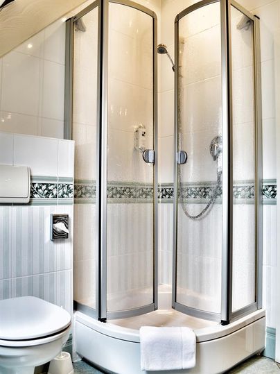 Ein modernes Badezimmer mit einer dreiseitigen Dusche und einer Toilette. Die Wände sind hell gefliest und es gibt einen Handtuchhalter.