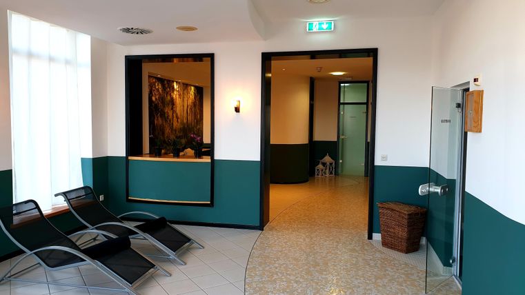 Een rustige wellnessruimte met ligstoelen en lichte muren. De receptie is goed zichtbaar, en er is toegang tot andere ruimtes.