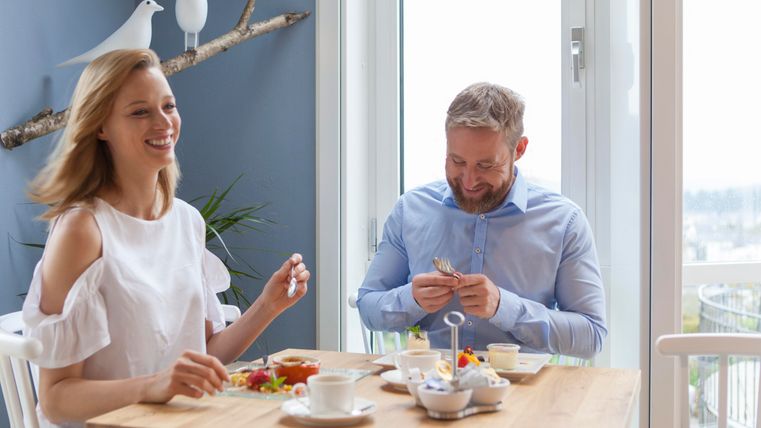 Ein Paar sitzt an einem Tisch und genießt ein Frühstück. Auf dem Tisch sind verschiedene Speisen und Getränke sowie eine helle, freundliche Umgebung.