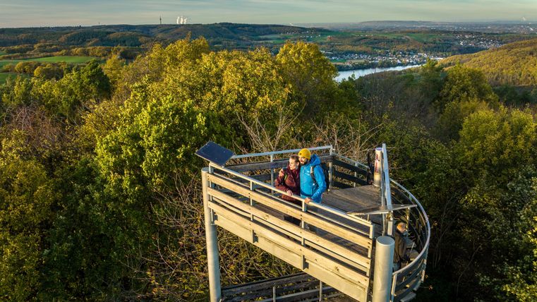 A viewpoint in nature with two people. In the background, lush forests and a river are visible.