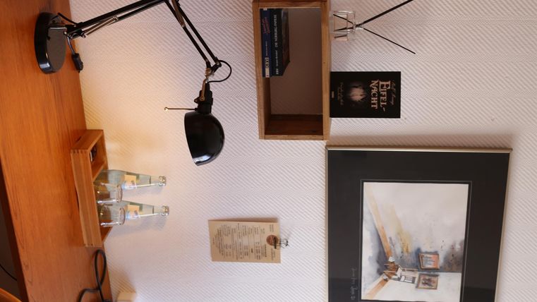 Ein gemütlicher Schreibtisch mit einer Lampe, Büchern und einem Gemälde an der Wand. Die Atmosphäre ist ruhig und einladend.