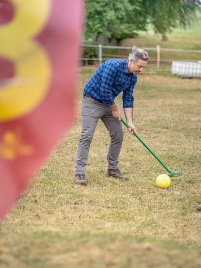 Een man staat op een weide en speelt met een grote gele bal. Op de achtergrond is een vlag zichtbaar.