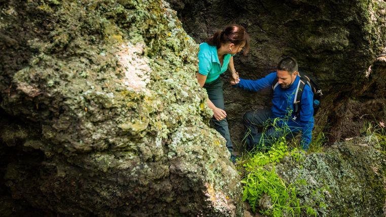 Een paar klimt over grote rotsen in de natuur. Ze helpen elkaar bij het overwinnen van obstakels.