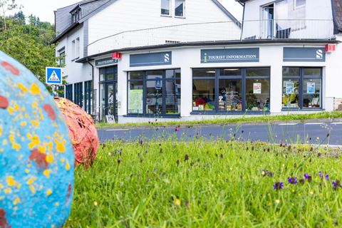 Eine Informationsstelle für Touristen mit großen Fenstern und einem einladenden Eingang. Im Vordergrund sind bunte, dekorative Kugeln auf grüner Wiese zu sehen.