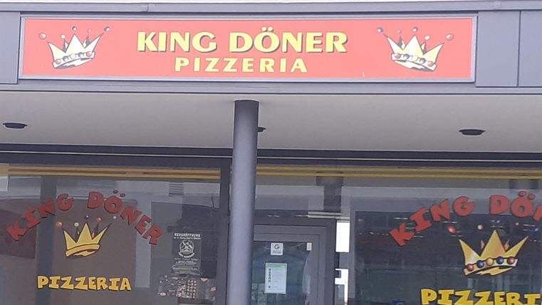 Ein Restaurant mit dem Namen "King Döner Pizzeria". Die Fassade zeigt ein rotes Schild mit einer Krone und den Worten "Döner" und "Pizzeria".