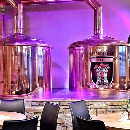 Twee grote koperen ketels voor de brouwerij staan voor een paarse verlichte muur. De ketel aan de linkerkant draagt het logo van een brouwerij.