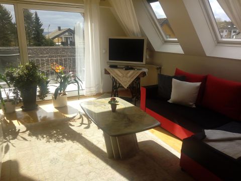 A bright living room with a red sofa and a coffee table. Large windows let in a lot of light and there are some plants in the room.
