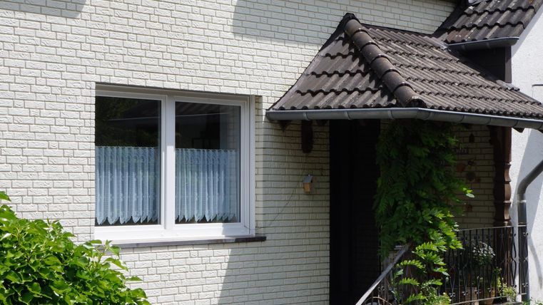 A cozy single-family home with a paved entrance. The garden is beautifully landscaped and decorated with various plants and flowers.