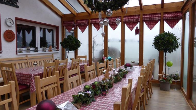 A bright conservatory with long wooden tables and chairs. The tables are festively decorated with Christmas decorations.