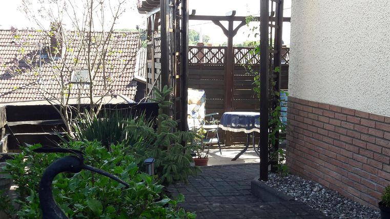 Een gezellige tuin met een poort en veel groen. Op de achtergrond zijn een tafel en stoelen te zien.