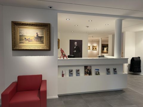 Ein moderner Empfangsbereich mit einem roten Sessel und einem Gemälde an der Wand. Auf dem Empfangstresen liegen Informationsbroschüren.