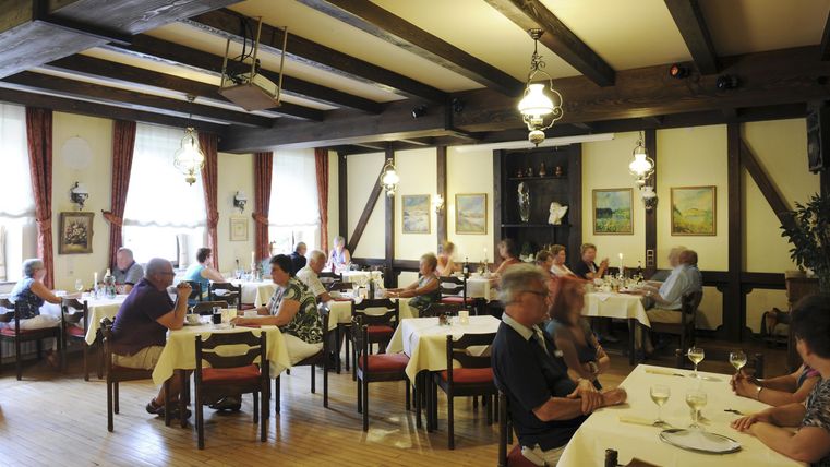Ein gemütliches Restaurant mit Holzbalken und Tischen. Gäste genießen ihre Mahlzeiten in einer einladenden Atmosphäre.