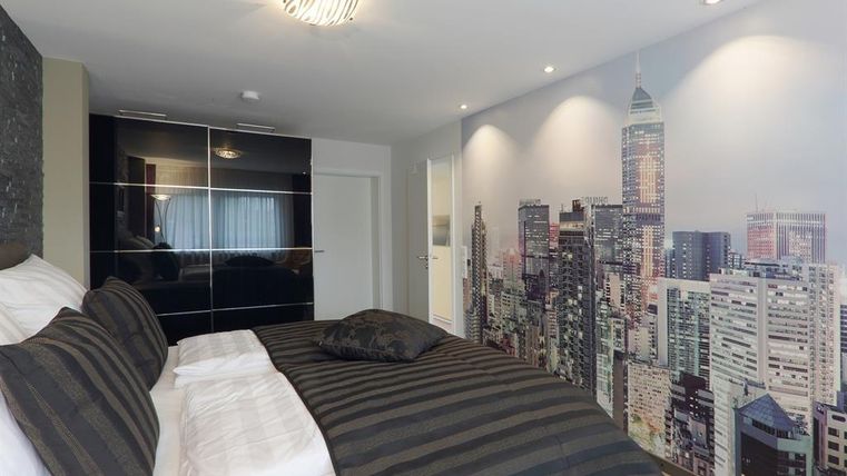 Een moderne slaapkamer met een bed in zwart en wit. De muur is versierd met een stadsbeeld van een skyline.