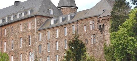 A historic building with a gray roof and stone facade. Surrounded by green trees and a picturesque landscape.