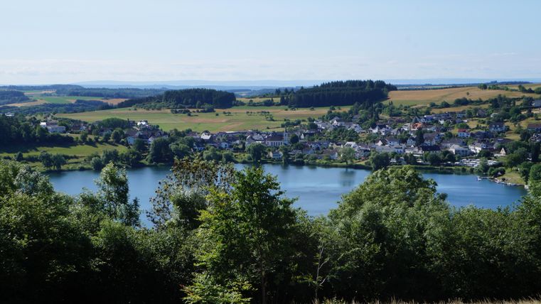 A quiet landscape with a lake and a small village.
Surrounded by green trees and gentle hills.