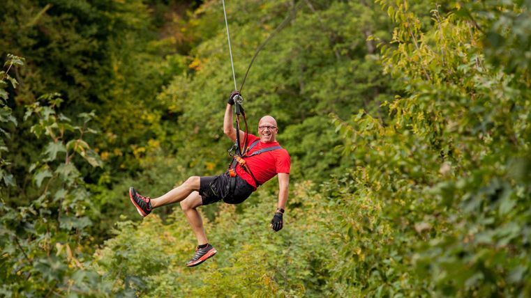 Laughing man hanging on a zipline in the forest