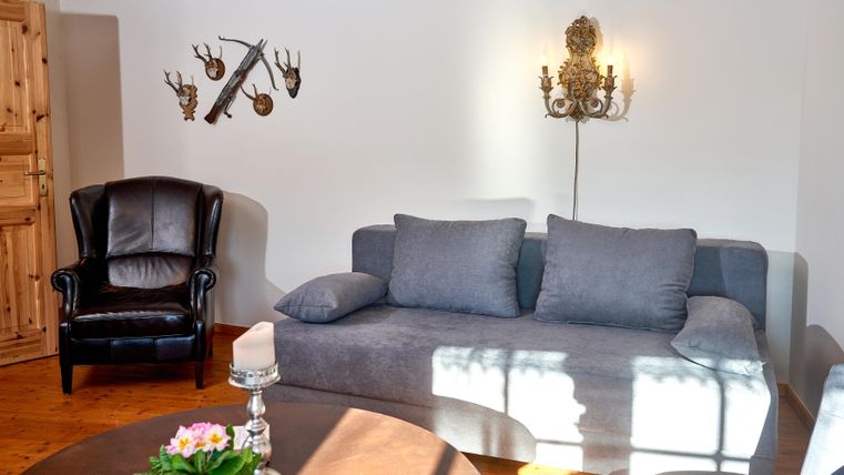 A modern living room with a gray sofa and a black armchair.
Decorative elements hang on the wall, and there is a table with a flower vase.
