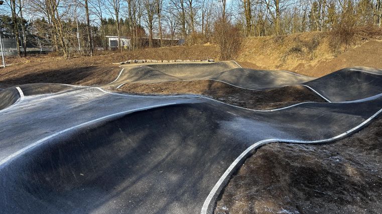 Een gepompte baan met gebogen bochten en een heldere blauwe lucht. De omgeving is omringd door bomen en ziet er rustig uit.
