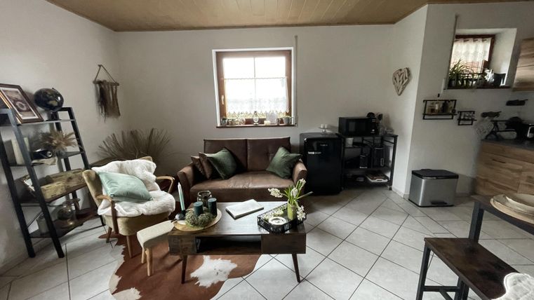 Een gezellige woonkamer met een bruine bank en een met hout bedekte tafel. Er zijn planten en decoratieve elementen aan de muren.