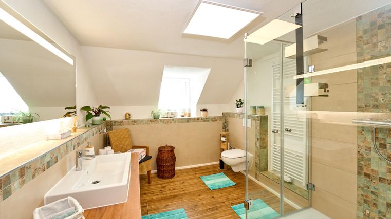 A modern bathroom with a large shower and a sink. The room has bright walls and an elegant wooden floor.