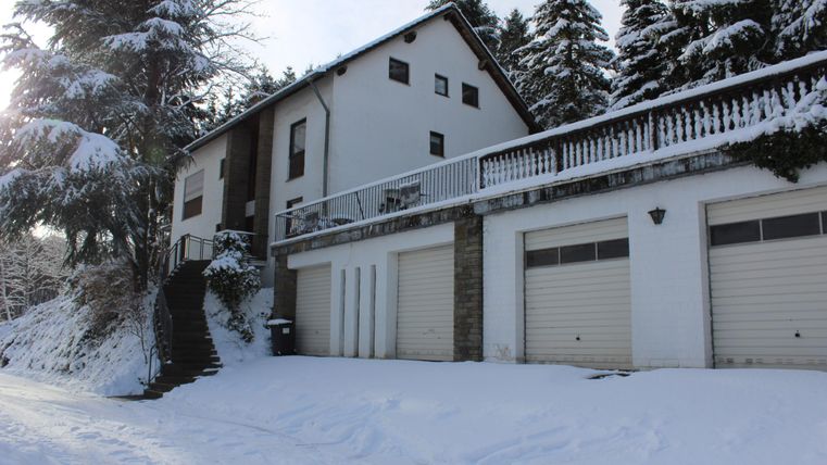 Ein modernes Haus in einer verschneiten Umgebung, umgeben von Bäumen. Der Schnee bedeckt den Boden und die Garagen im Vordergrund.